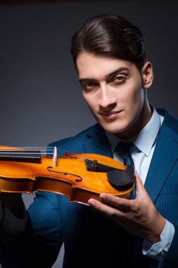 Genç adam karanlık odada keman çalıyor.