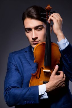 Genç adam karanlık odada keman çalıyor.