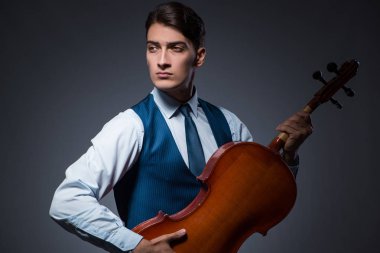 Genç adam karanlık odada çello çalıyor.