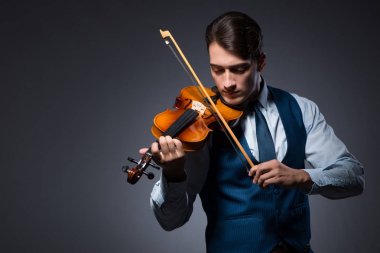 Genç adam karanlık odada keman çalıyor.