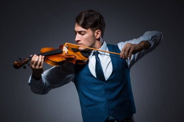 Genç adam karanlık odada keman çalıyor.