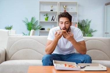 Pizza yiyen adam evde yemek yiyor, dinleniyor.