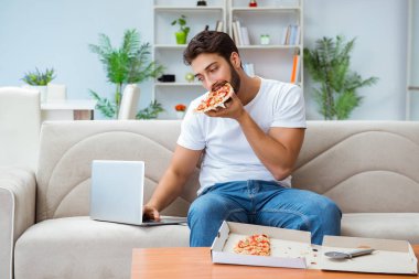 Pizza yiyen adam evde yemek yiyor, dinleniyor.