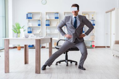 Ofiste egzersiz yapan işadamı VR gözlüğü takıyor.