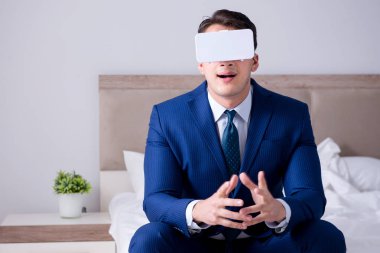 Yatak odasında sanal gerçeklik kulaklığı takan bir iş adamı.