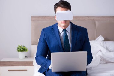 Yatak odasında sanal gerçeklik kulaklığı takan bir iş adamı.