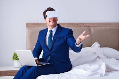 Yatak odasında sanal gerçeklik kulaklığı takan bir iş adamı.