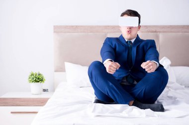 Yatak odasında sanal gerçeklik kulaklığı takan bir iş adamı.