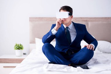 Yatak odasında sanal gerçeklik kulaklığı takan bir iş adamı.