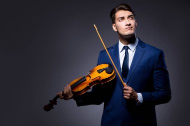 Genç adam karanlık odada keman çalıyor.