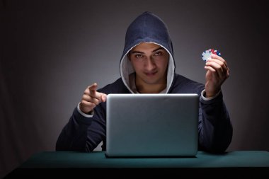 Kapüşonlu genç adam dizüstü bilgisayarın önünde oturuyor.