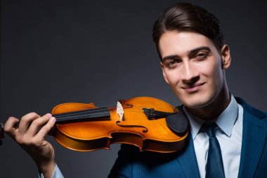 Genç adam karanlık odada keman çalıyor.