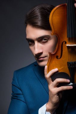 Genç adam karanlık odada keman çalıyor.