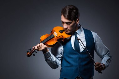 Genç adam karanlık odada keman çalıyor.