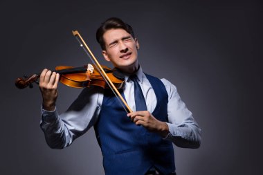 Genç adam karanlık odada keman çalıyor.