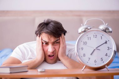 Yataktaki adam alarm yüzünden uykusuzluk çekiyor.