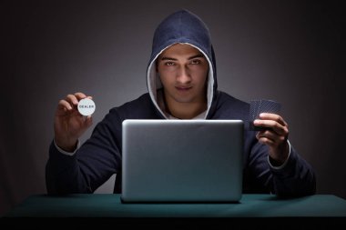 Kapüşonlu genç adam dizüstü bilgisayarın önünde oturuyor.