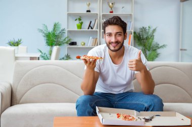 Pizza yiyen adam evde yemek yiyor, dinleniyor.
