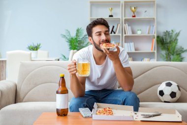 Pizza yiyen adam evde yemek yiyor, dinleniyor.