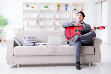 Evde gitar çalan bir iş adamı.