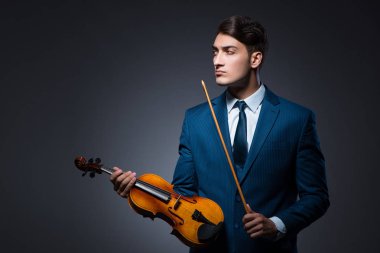 Genç adam karanlık odada keman çalıyor.