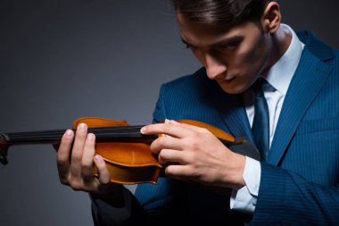 Genç adam karanlık odada keman çalıyor.