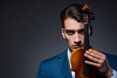 Genç adam karanlık odada keman çalıyor.