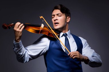 Genç adam karanlık odada keman çalıyor.