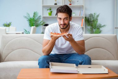Pizza yiyen adam evde yemek yiyor, dinleniyor.