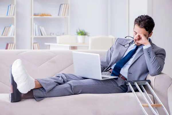 Zakenman met krukken en gebroken been thuis aan het werk — Stockfoto