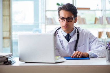 Hastane kliniğinde masasında oturan genç bir erkek doktor.