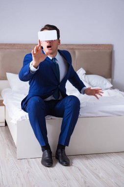 Yatak odasında sanal gerçeklik kulaklığı takan bir iş adamı.