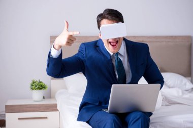 Yatak odasında sanal gerçeklik kulaklığı takan bir iş adamı.