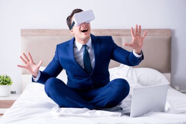 Yatak odasında sanal gerçeklik kulaklığı takan bir iş adamı.
