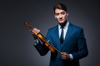 Genç adam karanlık odada keman çalıyor.