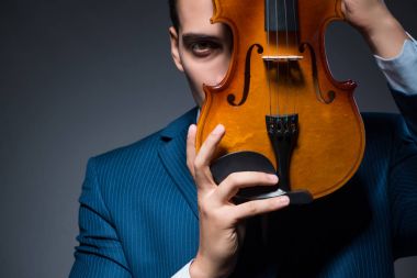 Genç adam karanlık odada keman çalıyor.