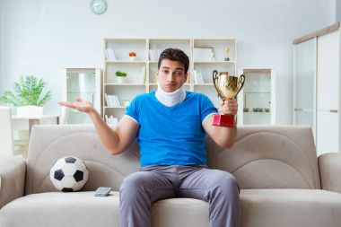 Boynundan sakatlanan bir adam evde futbol maçı izliyor.