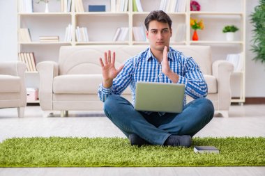 Genç yakışıklı adam evde yerde oturuyor.
