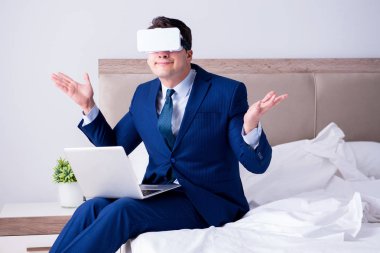 Yatak odasında sanal gerçeklik kulaklığı takan bir iş adamı.
