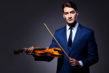 Genç adam karanlık odada keman çalıyor.