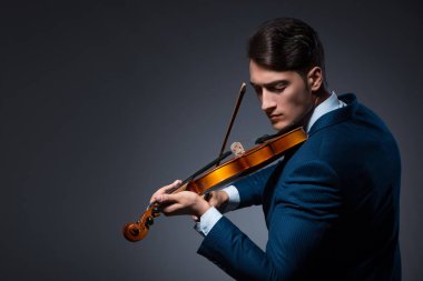 Genç adam karanlık odada keman çalıyor.