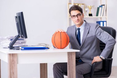 Genç işadamı tatilde ofiste basketbol oynuyor.