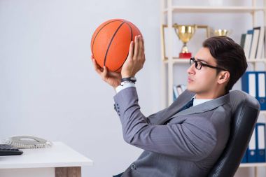 Genç işadamı tatilde ofiste basketbol oynuyor.