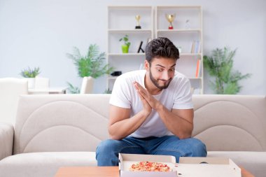 Pizza yiyen adam evde yemek yiyor, dinleniyor.