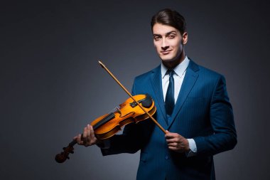 Genç adam karanlık odada keman çalıyor.