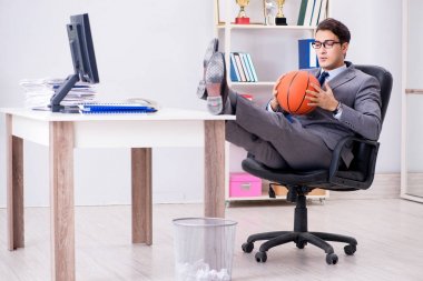 Genç işadamı tatilde ofiste basketbol oynuyor.