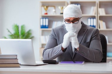 Bandajlı işadamı büroda kağıt işleriyle uğraşıyor.