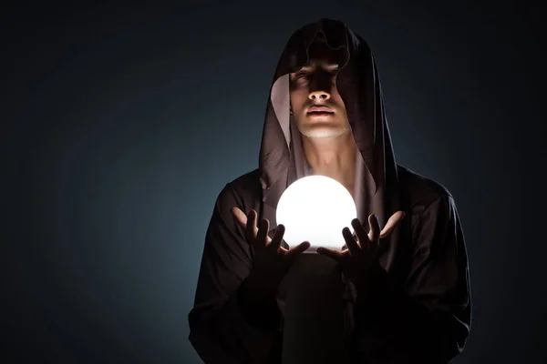 Молодой волшебник с хрустальным шаром в темной комнате — стоковое фото
