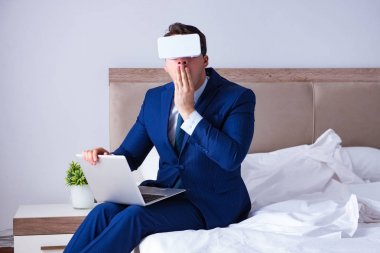 Yatak odasında sanal gerçeklik kulaklığı takan bir iş adamı.