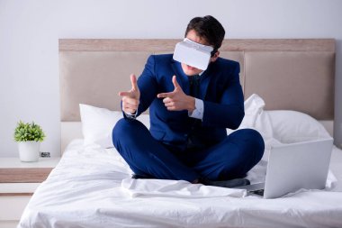 Yatak odasında sanal gerçeklik kulaklığı takan bir iş adamı.